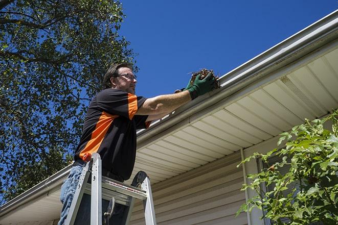 workman on a ladder repairing a broken gutter in Atlantic